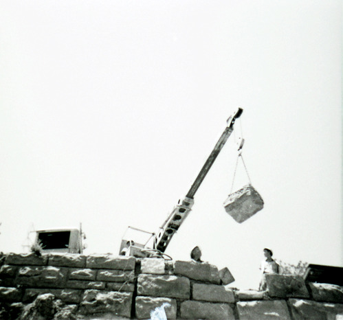 Men operating crane to lower rocks for repair of retaining wall along East Rim road.