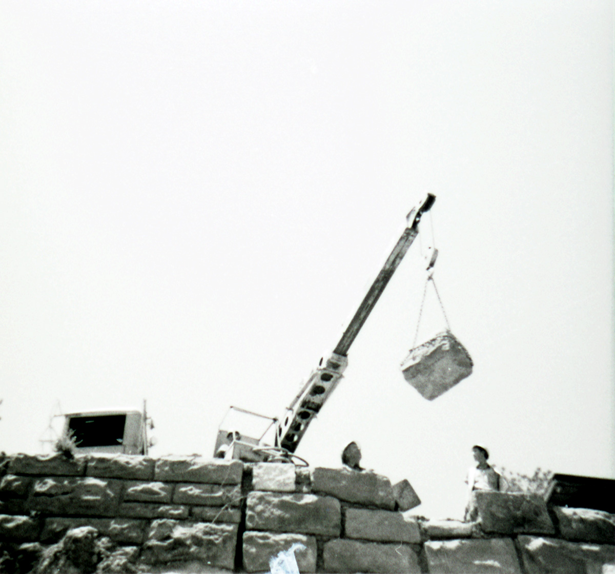 Men operating crane to lower rocks for repair of retaining wall along East Rim road.