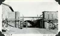 This is an historic black and white photograph from the Scotty's Castle Historic Photograph Collection, Death Valley National Park of Scotty's Castle Stables west entrance connecting wall with unidentified man. December 31, 1928. Photographed by Mat Roy Thompson.