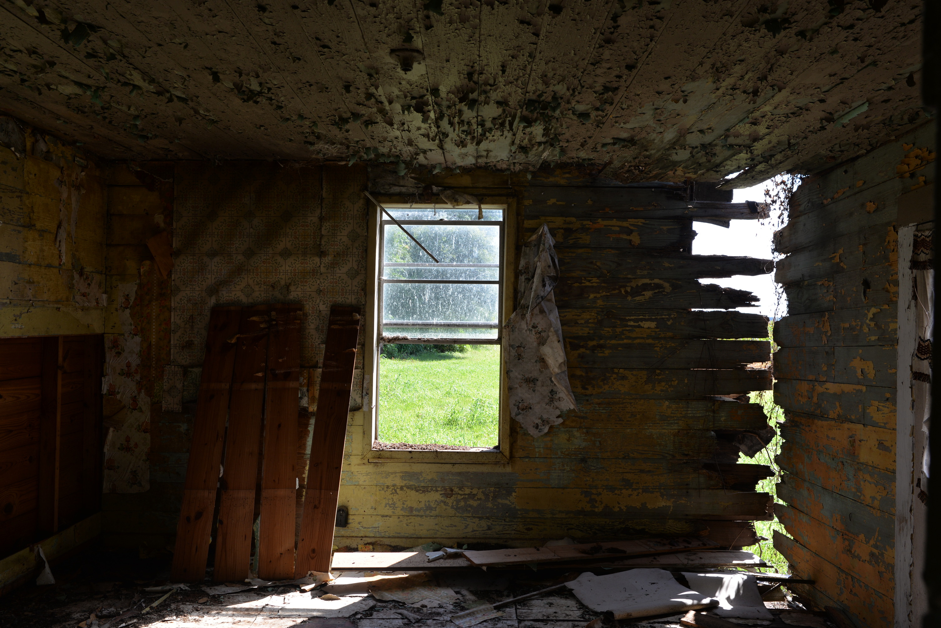 Wooden interior room with an open window and debris on the floor.