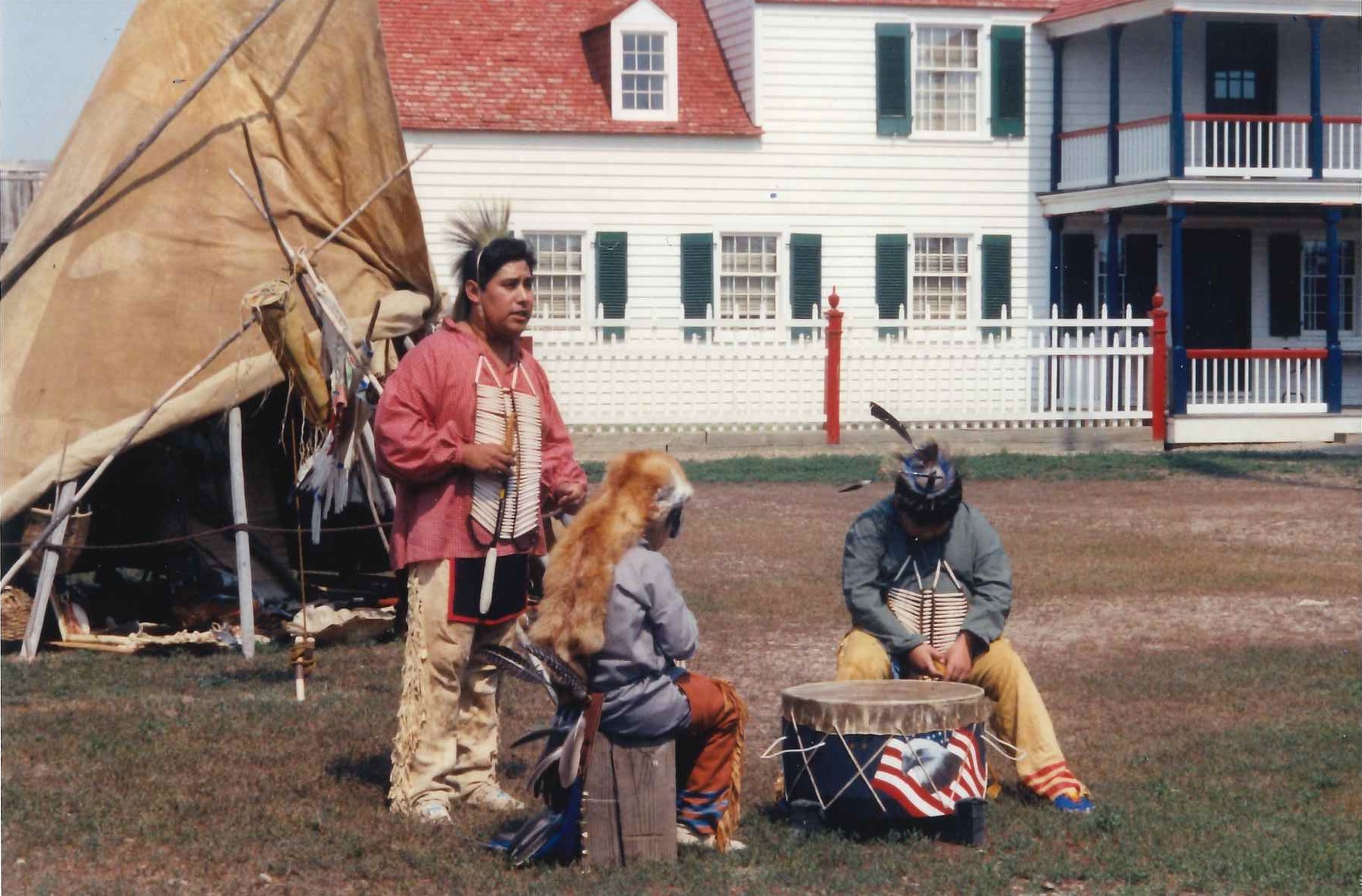 A man and two boys in traditional American Indian dress in front of a buffalo hide tipi