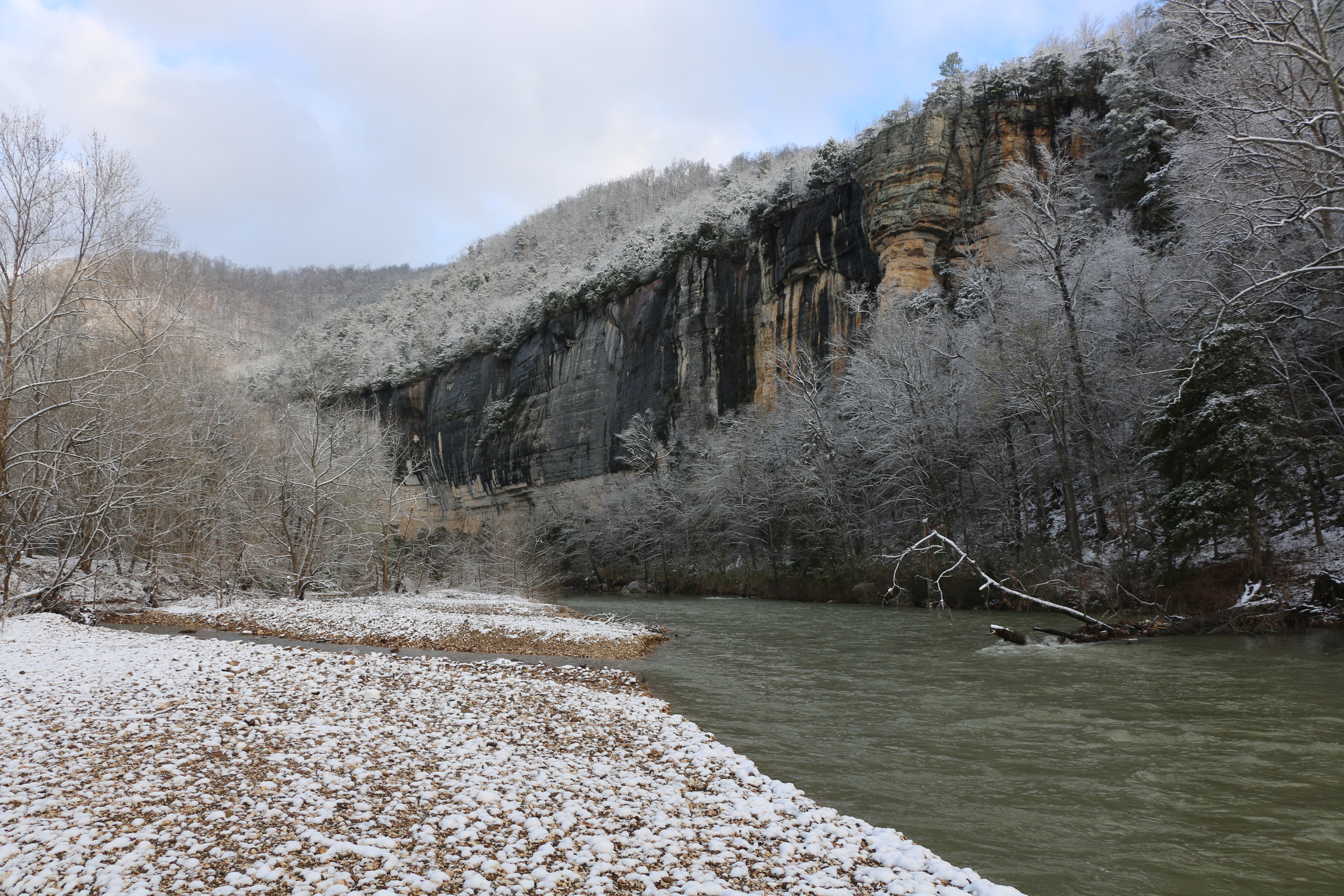 The Buffalo River runs muddy with snowy gravel bars and treetops on both banks.