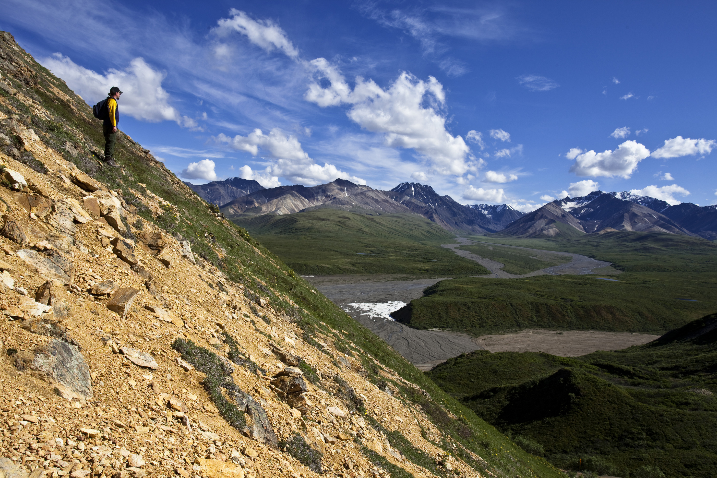 man standing on a steep mountainside, looking at a valley below