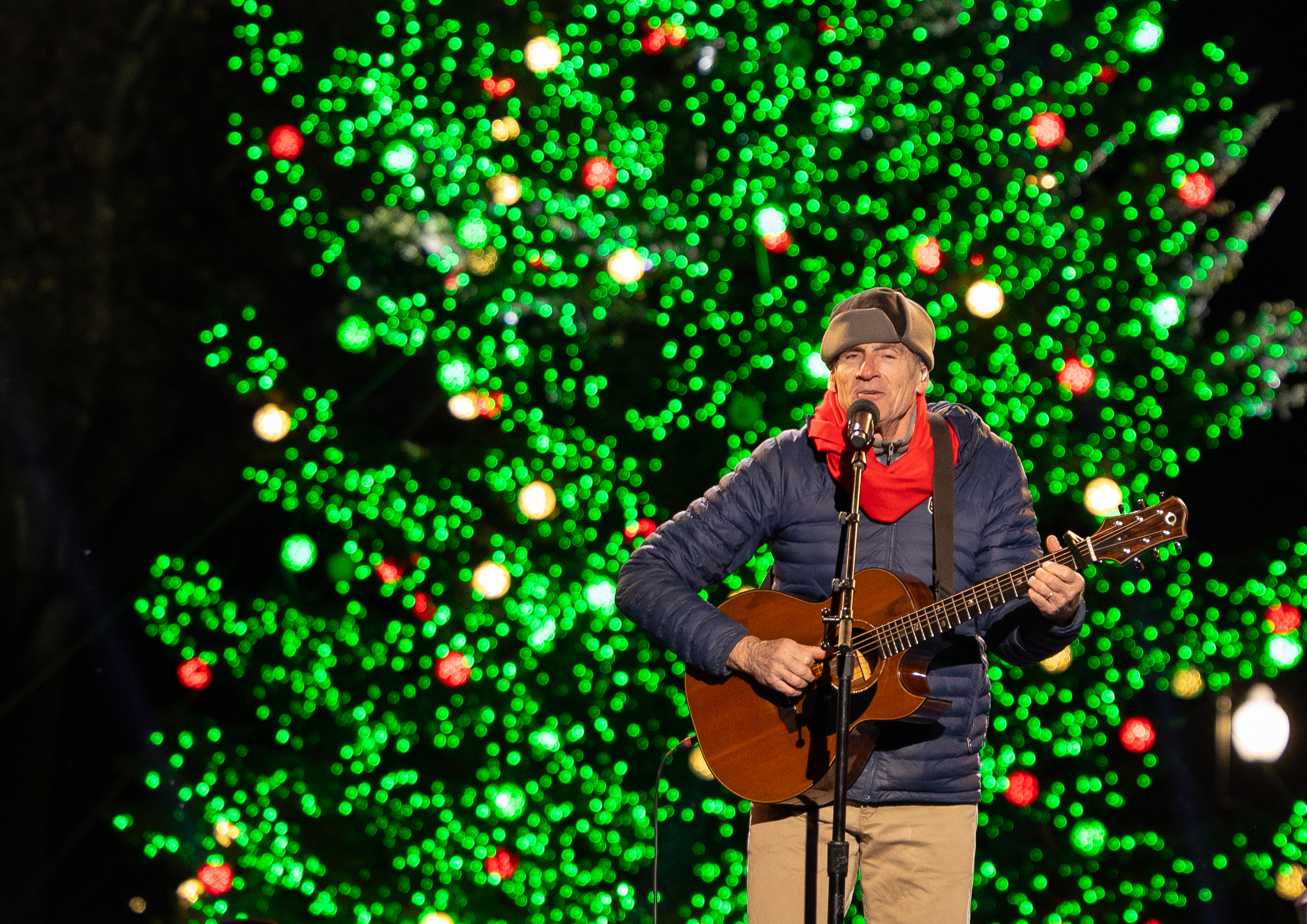 A man performs with a large Christmas Tree behind him