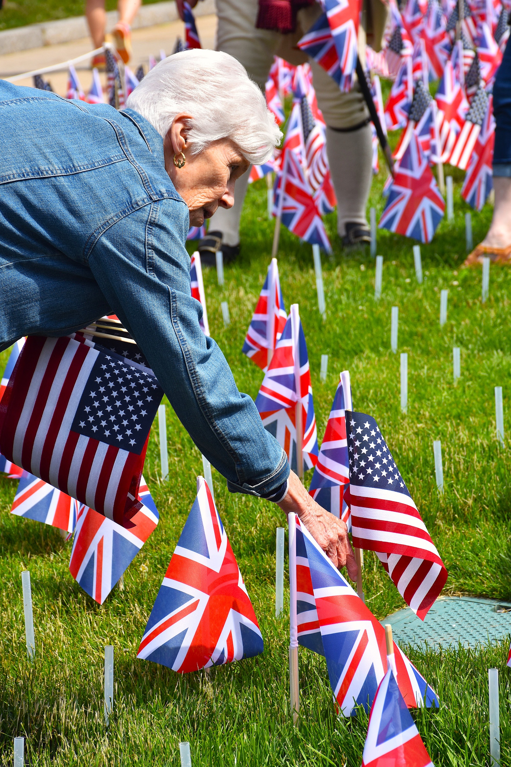 An older woman puts a US flag in a flag holder in the ground.