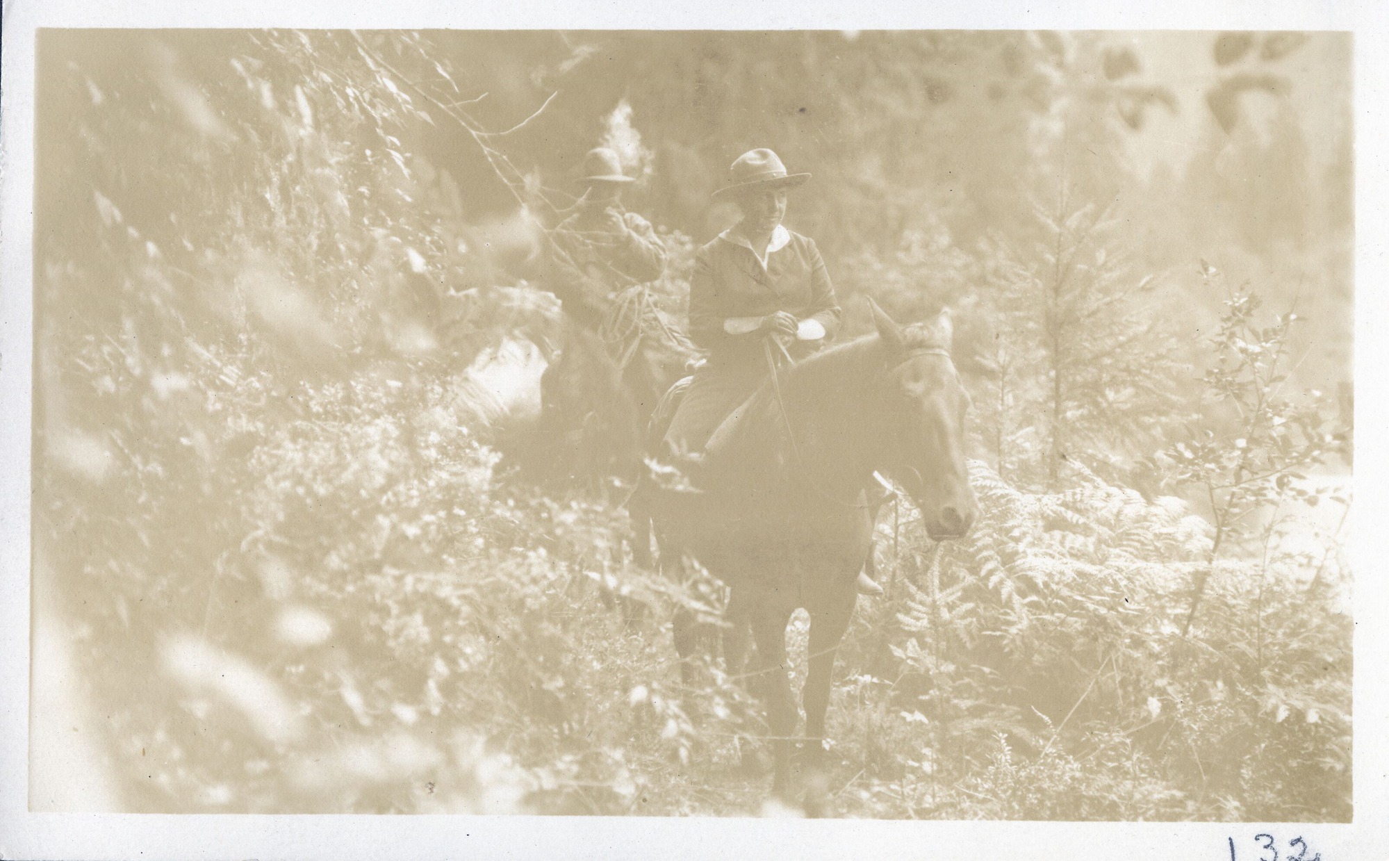 Mary Roberts Rinehart rides a horse through forest with a rider behind her.