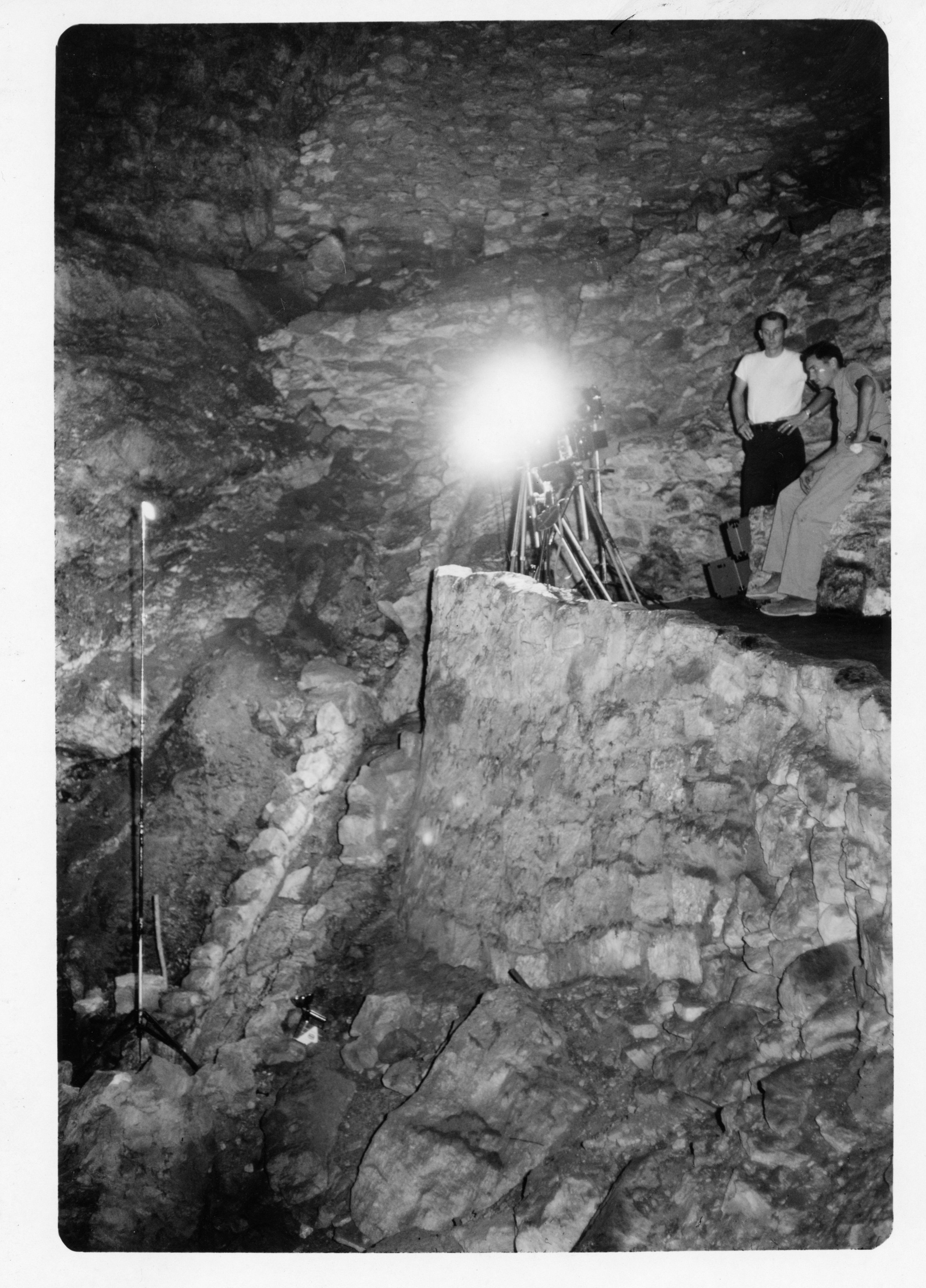 Black and white photograph of people taking another photograph with what looks to be a flash at night. The camera seems to be pointing down into the entrance. 