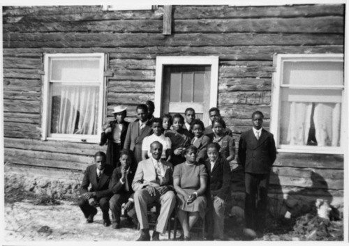 Large group of people in front of a large wood house.