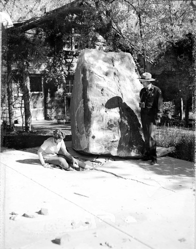 Rock fall behind Chief Ranger Fred Brueck's residence. Image shows house, rock, ranger, and woman sitting by rock fall depression.