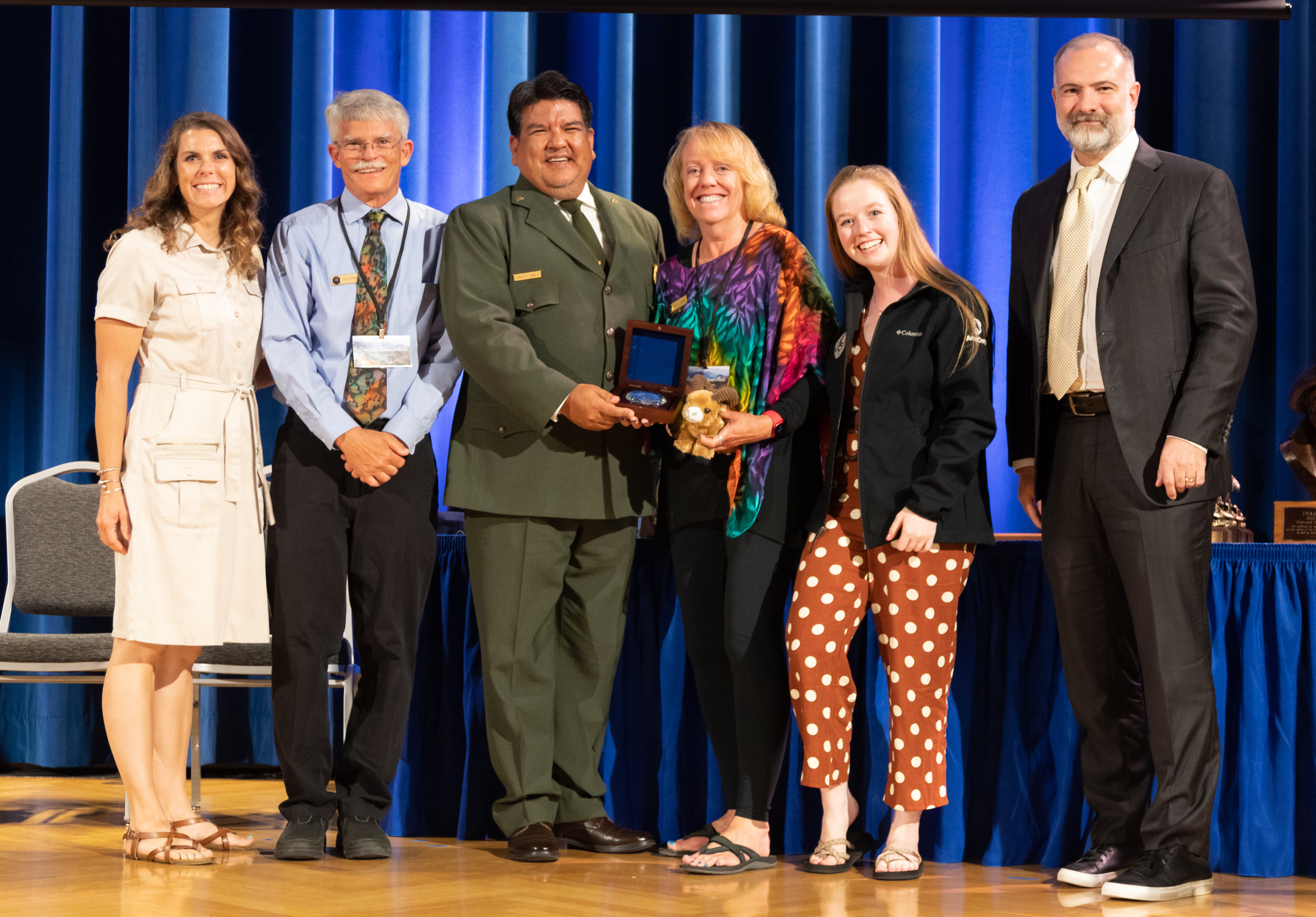 A group of six people smile as they accept an award on stage with the Director of the National Park Service. 