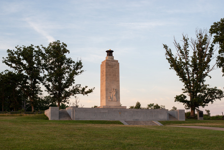 A stone monument with rectangular platform base that people can walk on and a 50 foot tall rectangular shaft with a light on top.