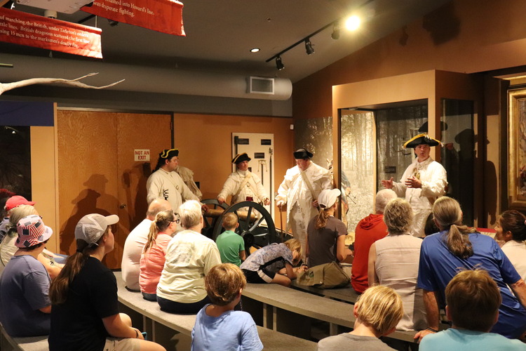 The Kingsbury Artillery describing the parts of a Grasshopper cannon during a weapons talk. The men are wearing period clothing and have tricorn hats with yellow brims.