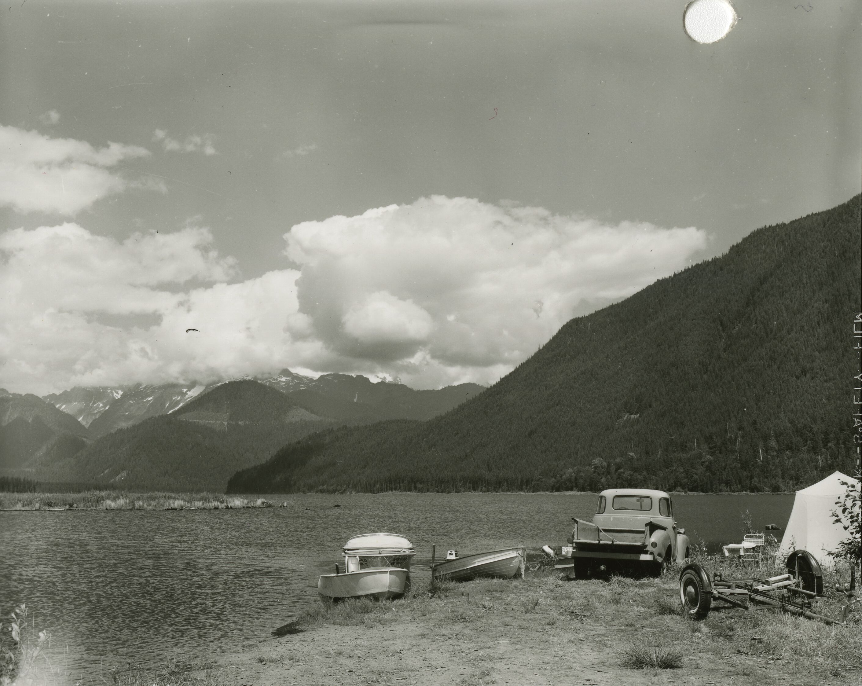 Two boats, a truck, and a tent on the shore of a lake.