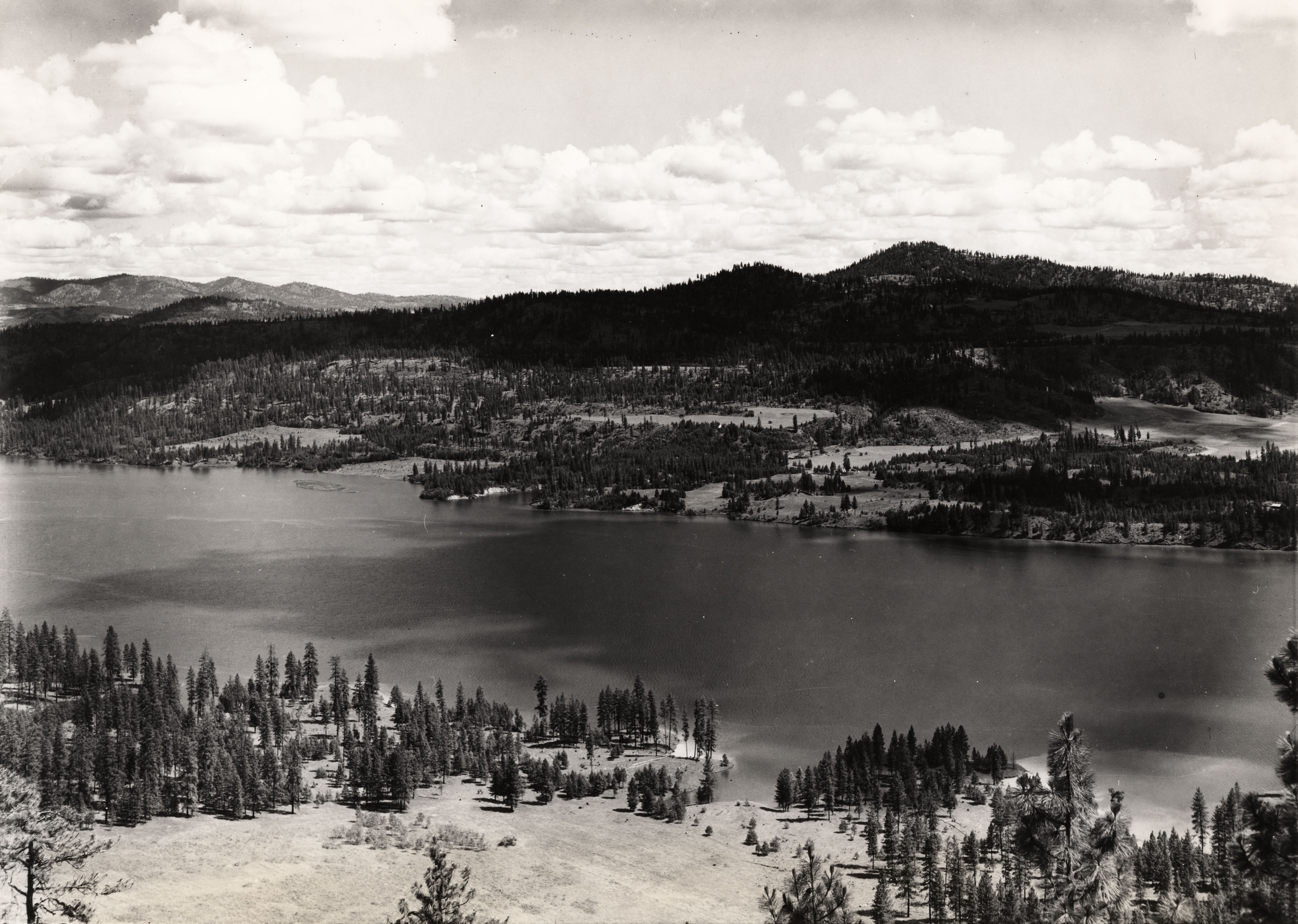 Black and white photograph of a a body of water in a wide forested valley 