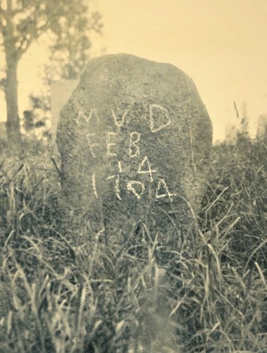 Light grey gravestone, with inscription. Grass and a tree are also visible. 