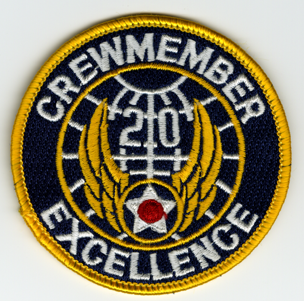 Circular, dark blue with yellow border. Inside yellow border stitched in white CREWMEMBER / EXCELLENCE" with another yellow border inside with the 20th Air Force symbol inside that: white grid with white "20" towards top and gold wings beneath. At joint between wings is yellow circle  dark blue inside with white 5-point star and red center."

