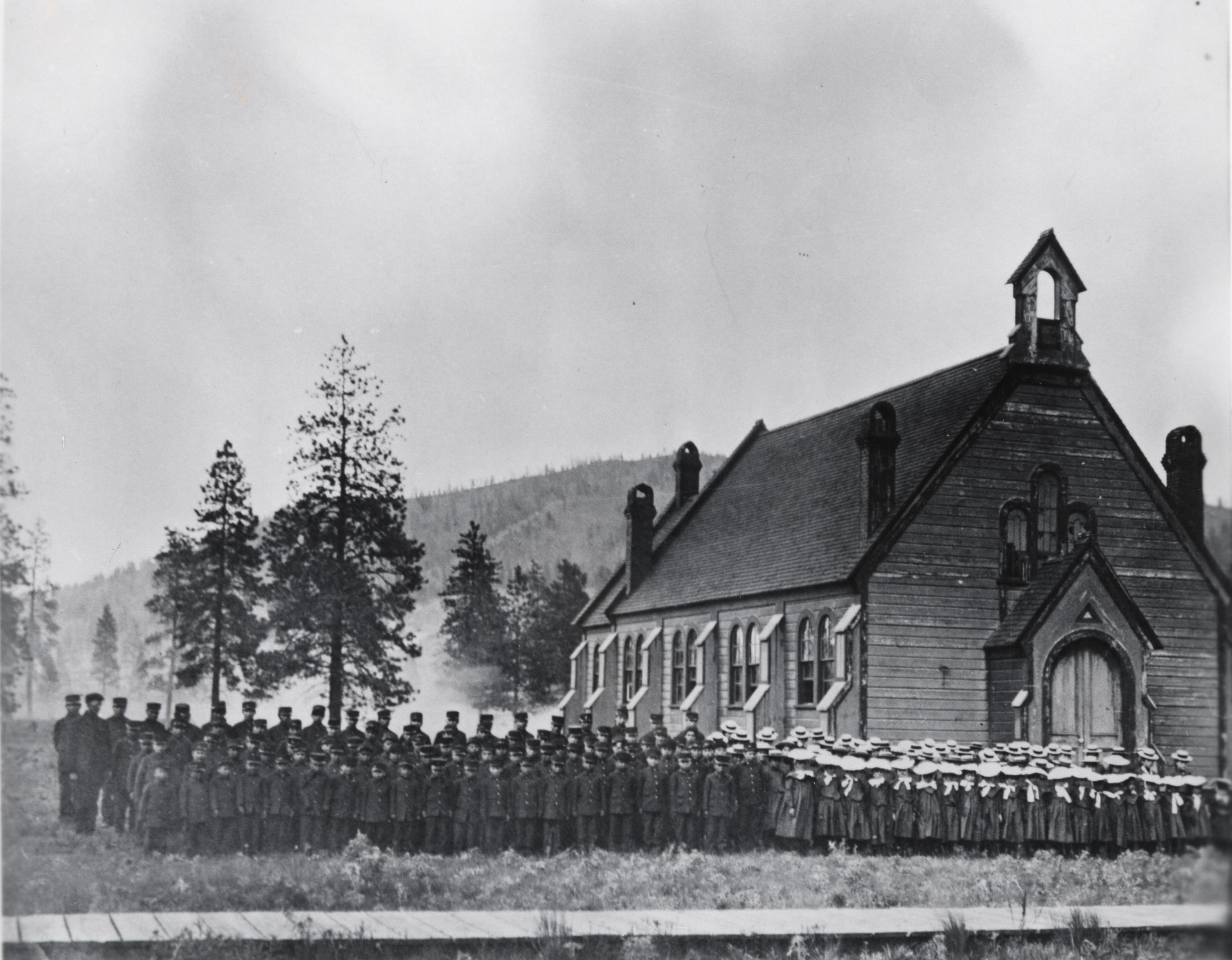 Black and white photograph of rows identically dressed students standing in front of chapel