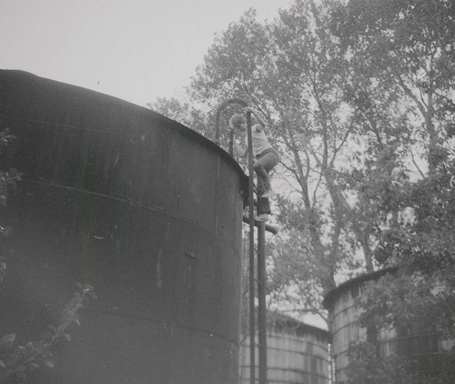 Woman climbing ladder of water tank prior to start of reroofing project.