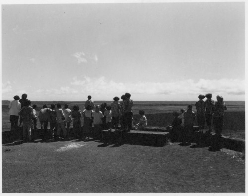 Black and white. Group of people with their backs to the camera looking at at crater from an overlook
