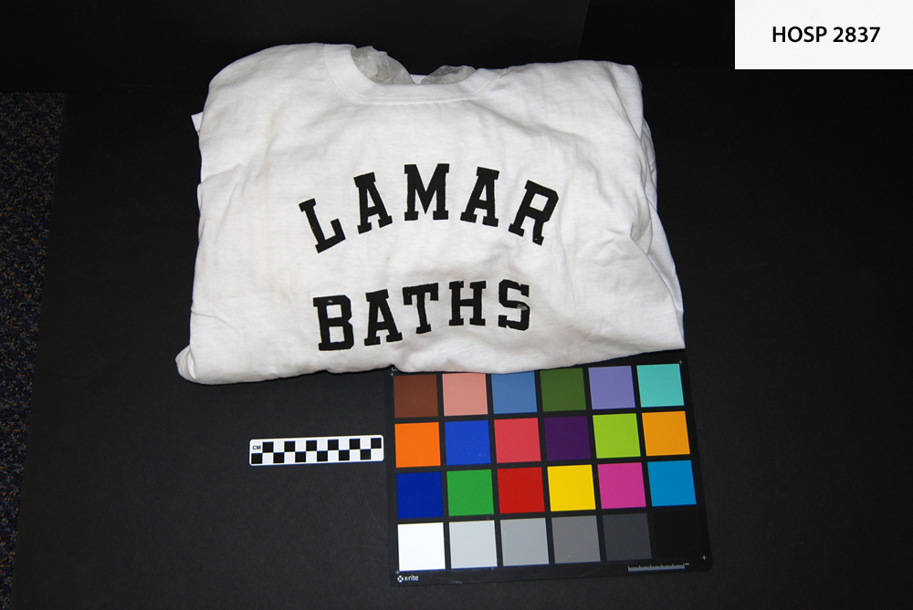 Man's cotton T-shirt; White, man's size XL, short sleeved, crew neck; Printed in black on front, "LAMAR BATHS"; white label in back embroidered in red reads "WILTON 100% COTTON  XL"; worn by male bath attendants in Lamar Bathhouse; Somewhat soiled along old fold lines.