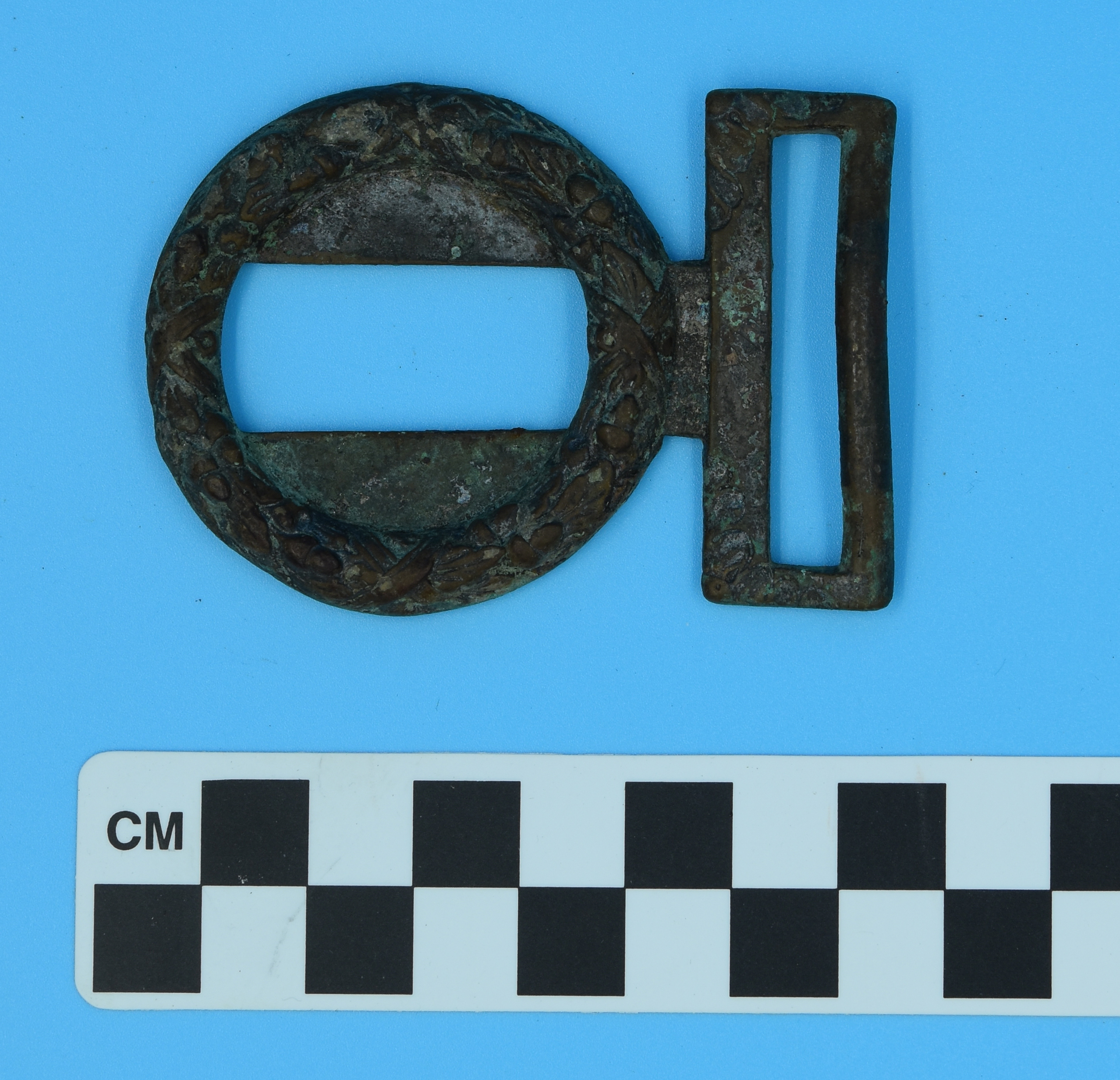 A silver metal belt buckle in the shape of a circle with a slot in the center. On one side is a rectangular loop.