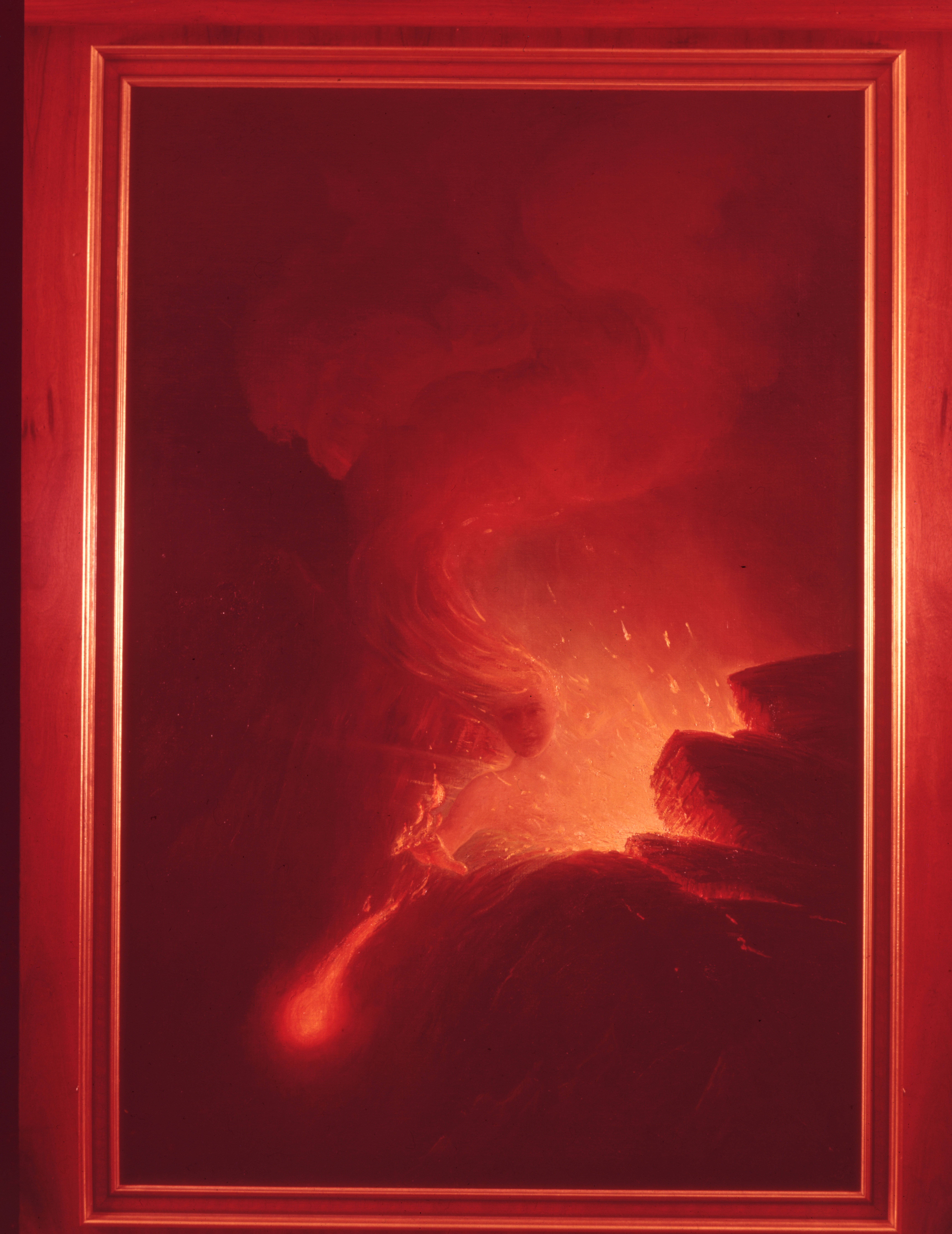 A red tinted image of David Howard Hitchcock's painting titled, "Madame Pele."  Pele is seen emerging between two cliff edges. Her face is looking towards the viewer of the painting. Her right arm and hand are stretched out. A ball of flames is shooting out of her right hand. Her hair is blowing towards the left side of the image. Her hair looks like a stream of lava and ends in a large puff of smoke. Near Pele's left shoulder and chest is an orange glow with orange sparks going towards the sky. The painting is in a wooden frame.