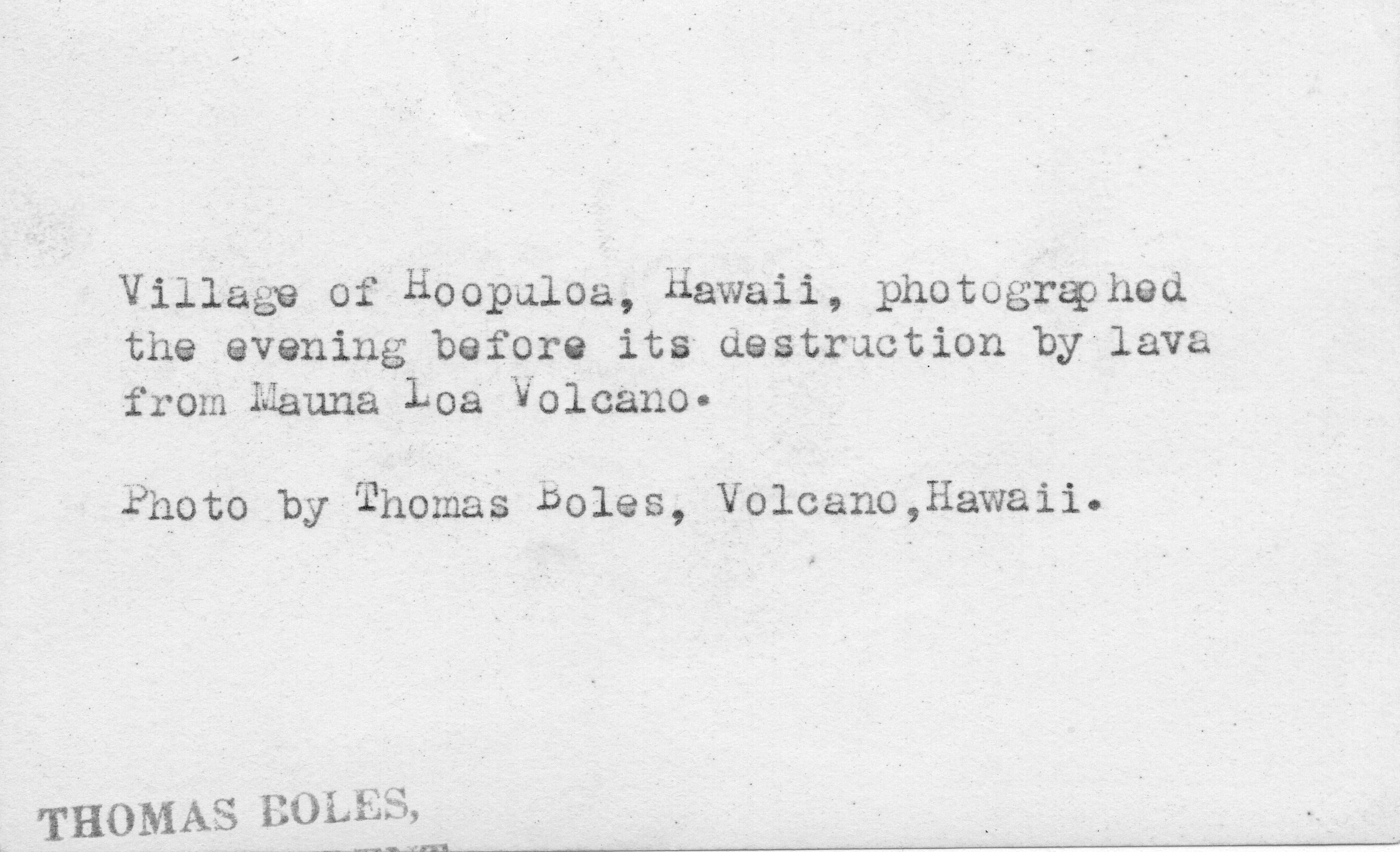 The image is in black and white. A label at the center of the photo reads, "Village of Hoʻōpūloa, Hawaiʻi, photographed the evening before its destruction by lava from Mauna Loa Volcano." A space below, another label credits the photographer; "Photo by Thomas Boles, Volcano, Hawaii."  A stamp in the lower left corner of the picture reads, "Thomas Boles," in capital letters.