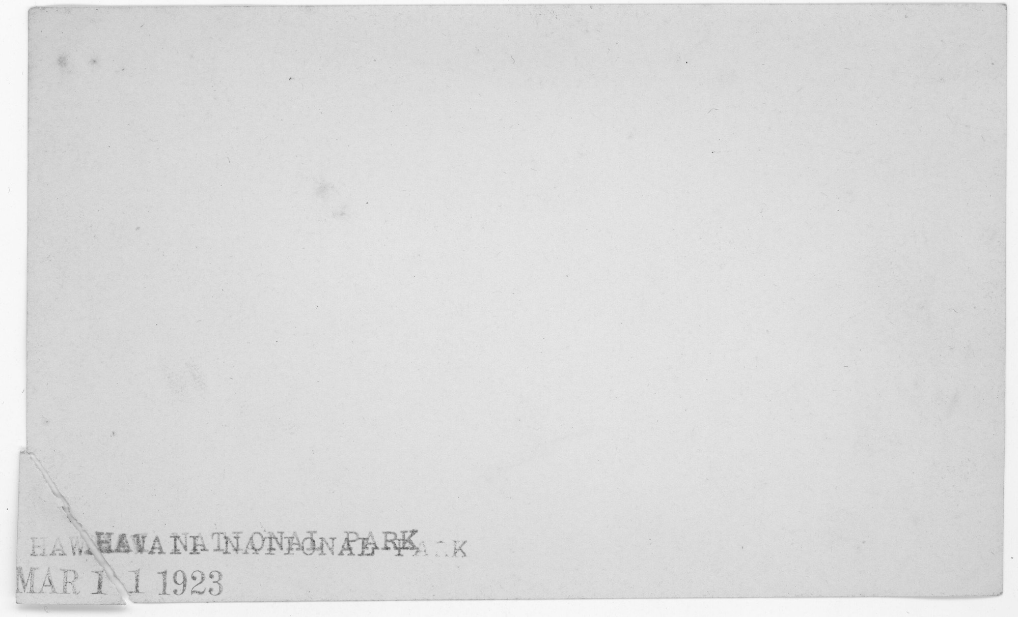 Reverse side of a photogrpah, "Hawaii National Park" is stamped mulitple times on the bottom left side. The bottom left corner is torn off and unattached. "Mar 11 1923" is stamped along the teared edge.