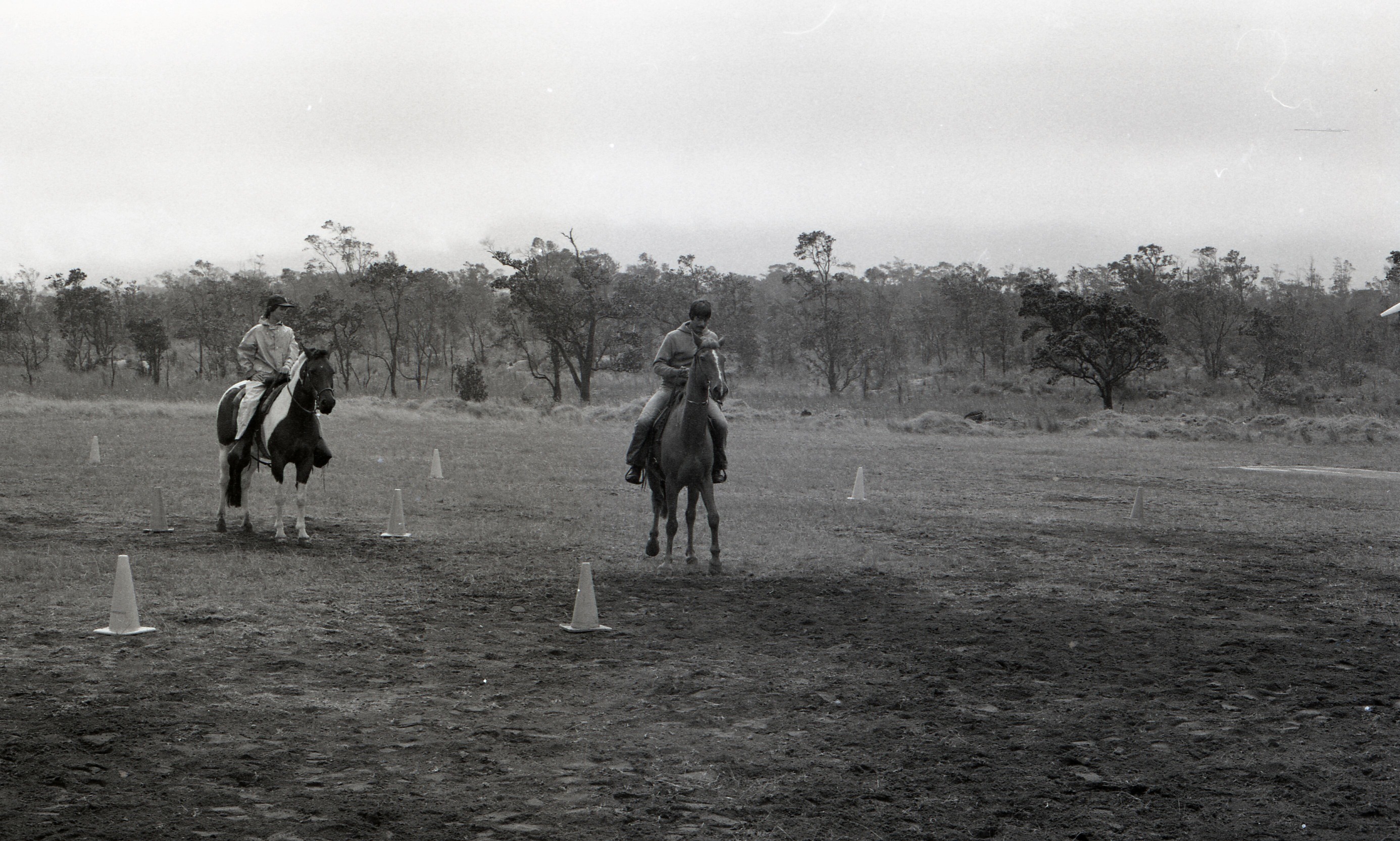 A black and white image of two men on horse back in a ball field at Kilauea Military Camp. There are eight cones surrounding the two men on horses.