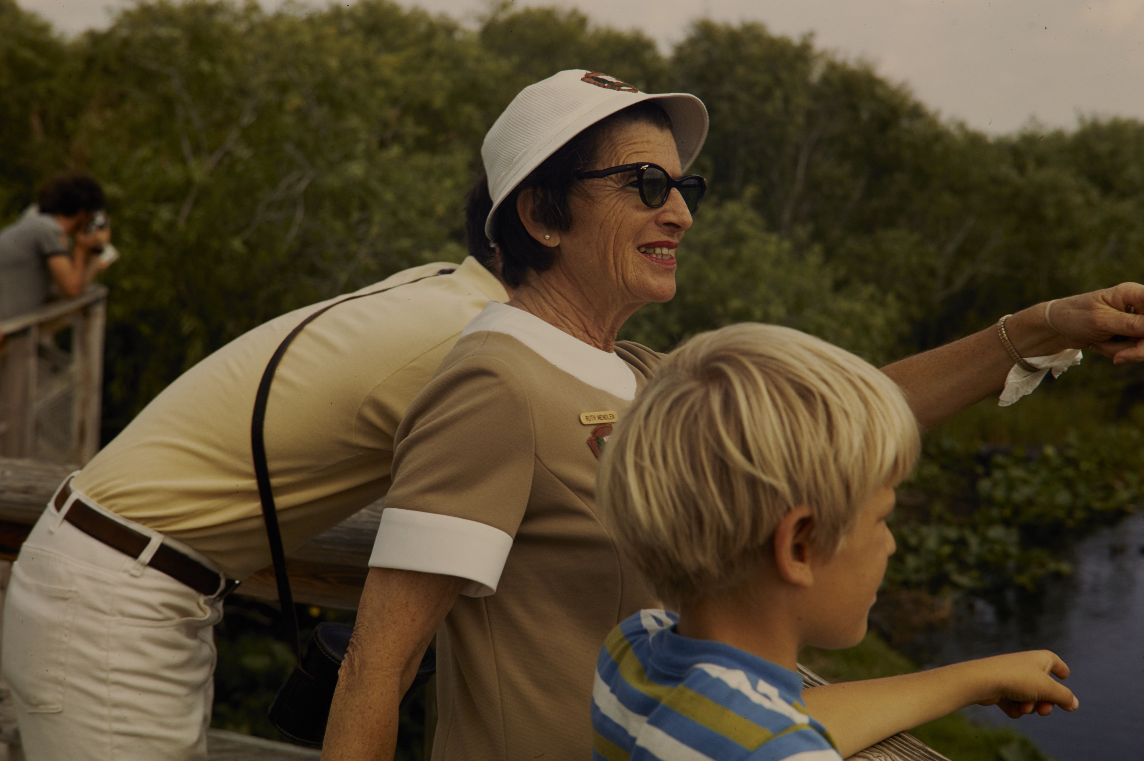 Ruth Mendlen in her NPS uniform stands between a boy and a man and points out towards something unseen in the water. 