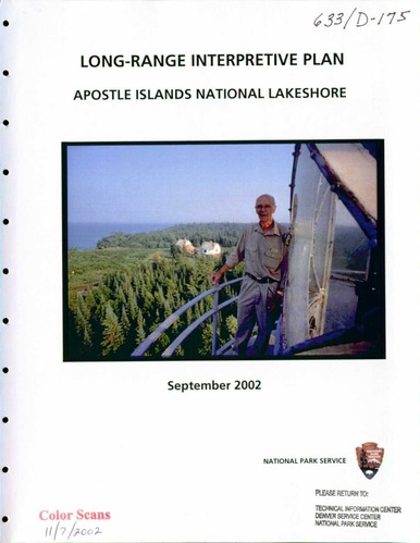 A man with white hair and glasses wearing a tab shirt and pants stands outside a lighthouse looking at us