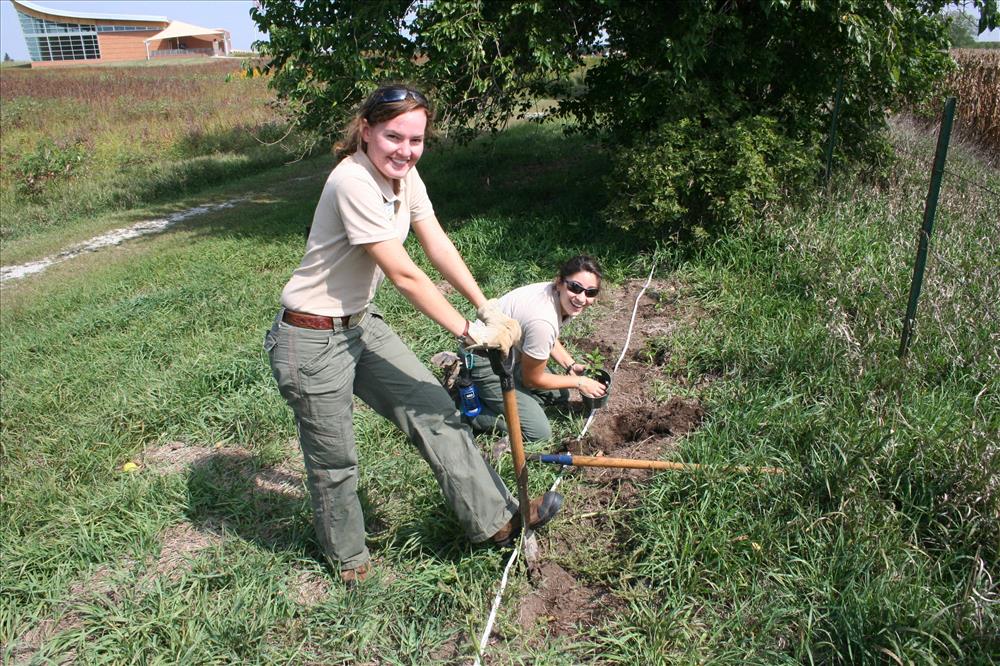 Two SCA interns work on digging up an area near the fence line.