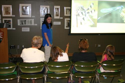 A SCA intern is giving a PowerPoint program about insects to a group of people of various ages.