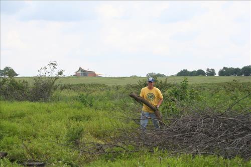 A YCC member holding a large branch next to a pile of brush.