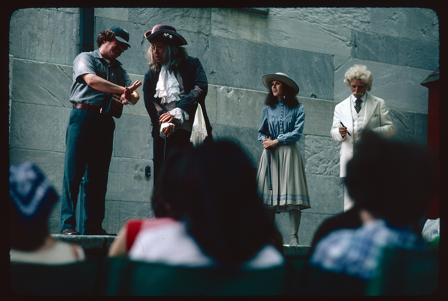 Second Bank of the United States. Exterior. Looking northwest from the left (east) side, near the rear face. Play performance of "We've Come Back for a Little Look Around" by Daniel M Klein. All the characters looking at a photo. Maintenance worker character talking to Benjamin Franklin, with Annie Oakley and Mark Twain to the right.