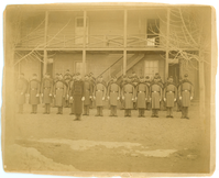 Men in Long Jackets Holding Rifles with Fixed Bayonet in Front of a Barracks Building