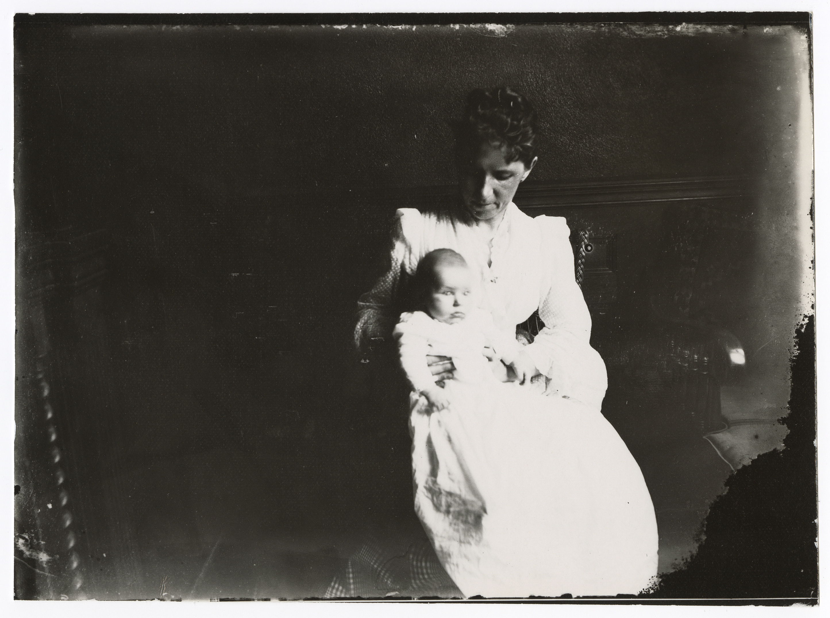A white woman wearing all white sits and holds a baby.