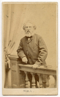 Henry Wadsworth Longfellow standing behind balustrade with his right arm leaning on a pillar. He is holding the balustrade with his left hand near a book. A draped curtain is visible in the left background. Longfellow is wearing formal clothes and has ear-length hair and a graying beard.