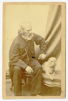 Henry Wadsworth Longfellow is sitting on a chair and is turned partially to his left. He sits next to a small shaggy dog that is lying on a stool or couch. Drapery is visible in the right background. Longfellow has chin-length graying hair and a mid-length graying beard.