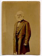 Half-length portrait of Henry Wadsworth Longfellow standing at three-quarter profile to his right. He holds a cane at his right side. A faint indication of a window is in left background. Longfellow wears formal attire with a long coat and has ear-length white hair and a full white beard.