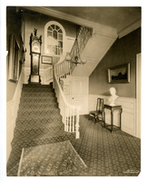 Black and white photograph of white paneled staircase with Grandfather clock on landing.