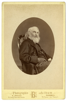 Henry Wadsworth Longfellow seated, facing three-quarter view to viewer's right. Image in oval. Longfellow is wearing dark vest and jacket and striped trousers. He has almost shoulder-length white hair and a full white/gray beard.