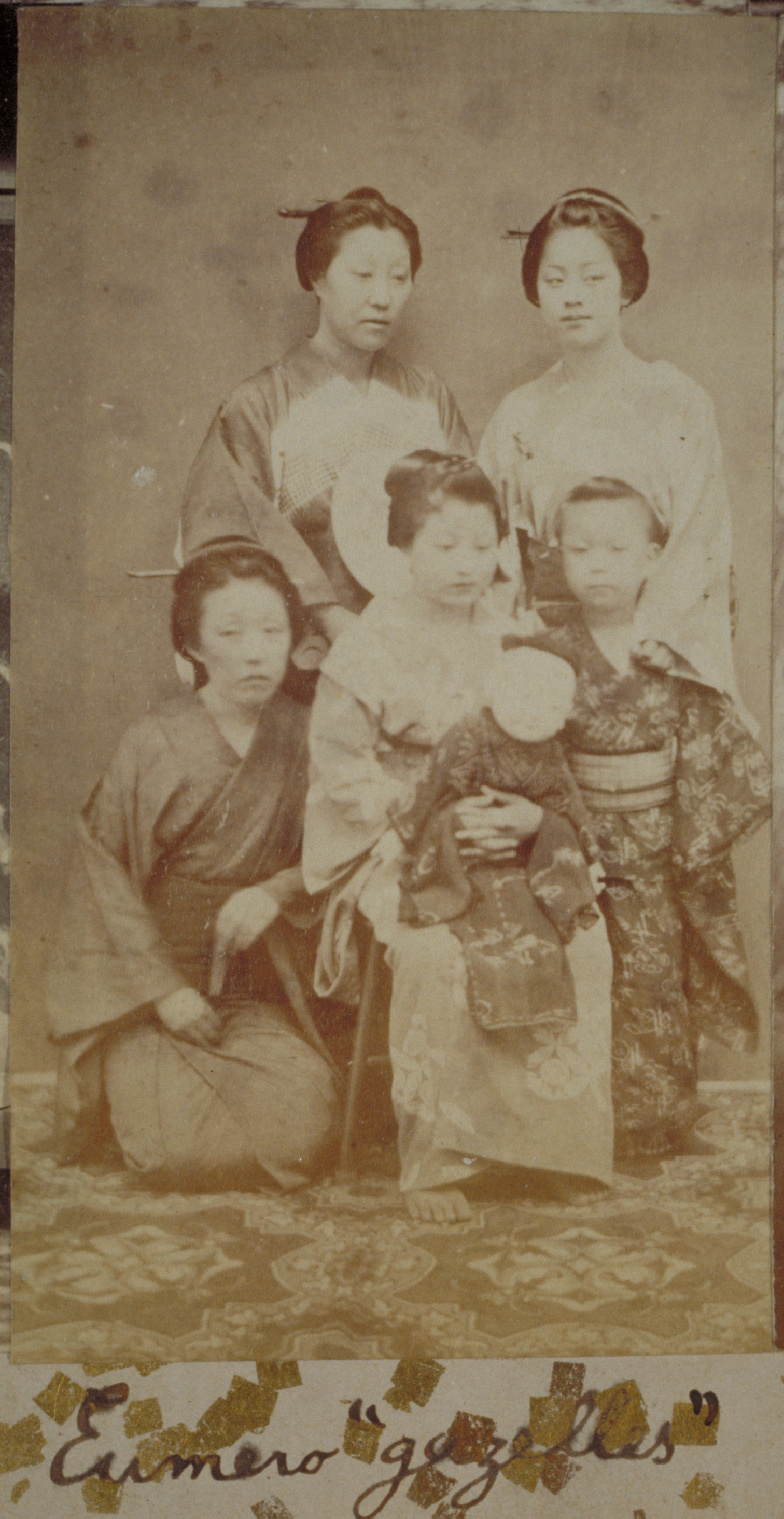 Black-and-white photograph representing Japanese women, two standing and one sitting, and two standing Japanese girls, all close to each other, one girl holding a doll