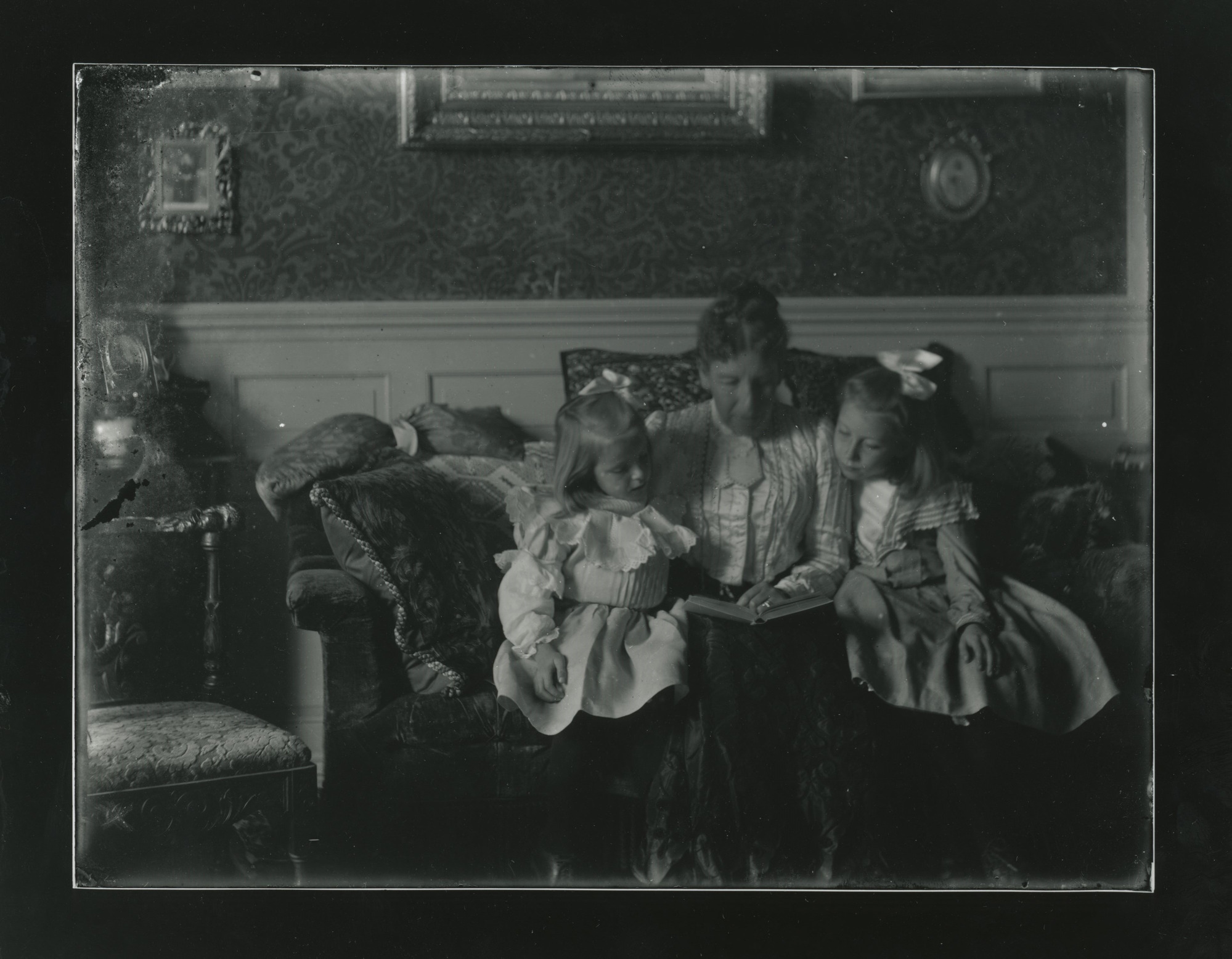 A white woman sits and reads on a couch in between two young girls.