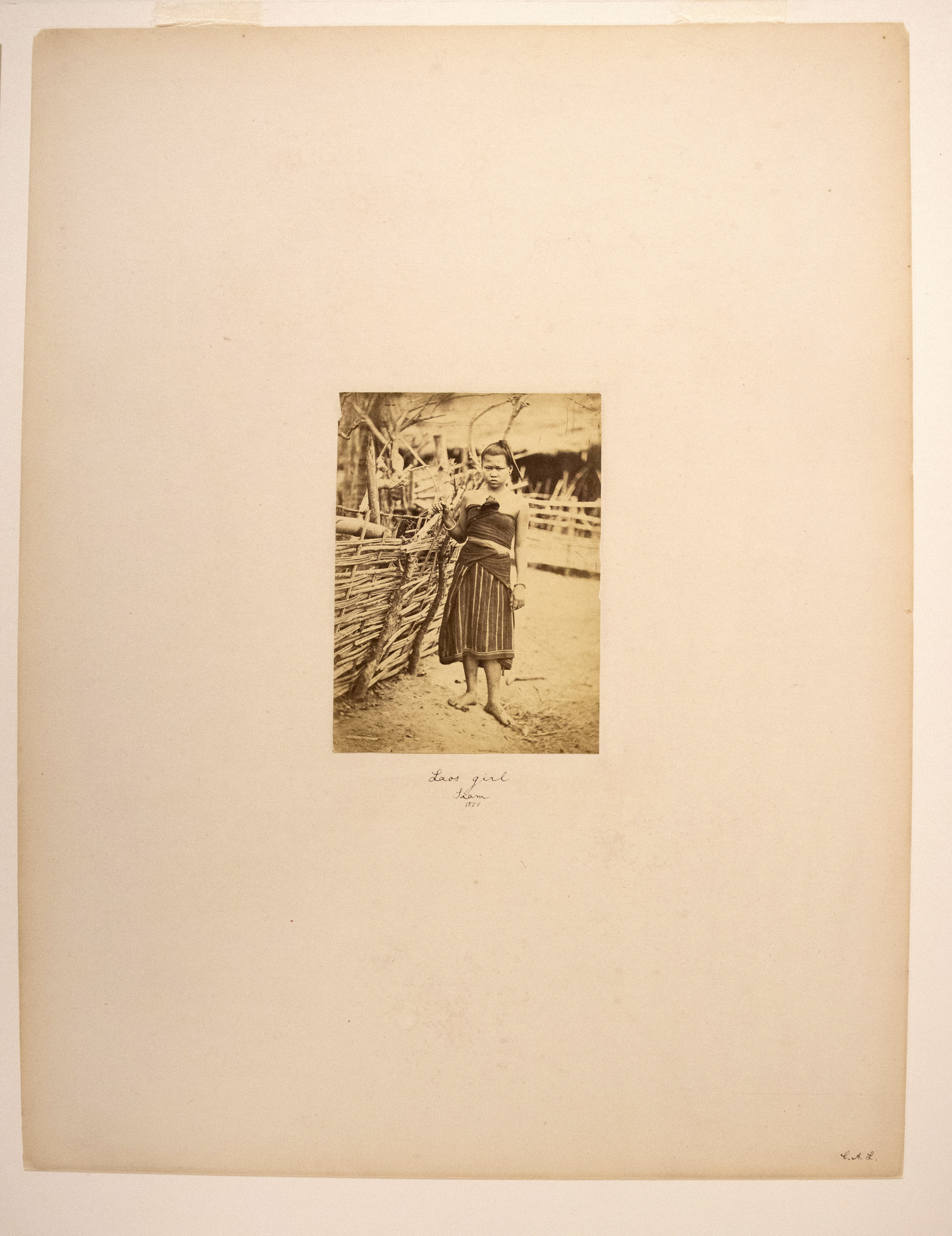 Sepia photograph with an inscription representing a Laotian girl standing by a wooden fence.