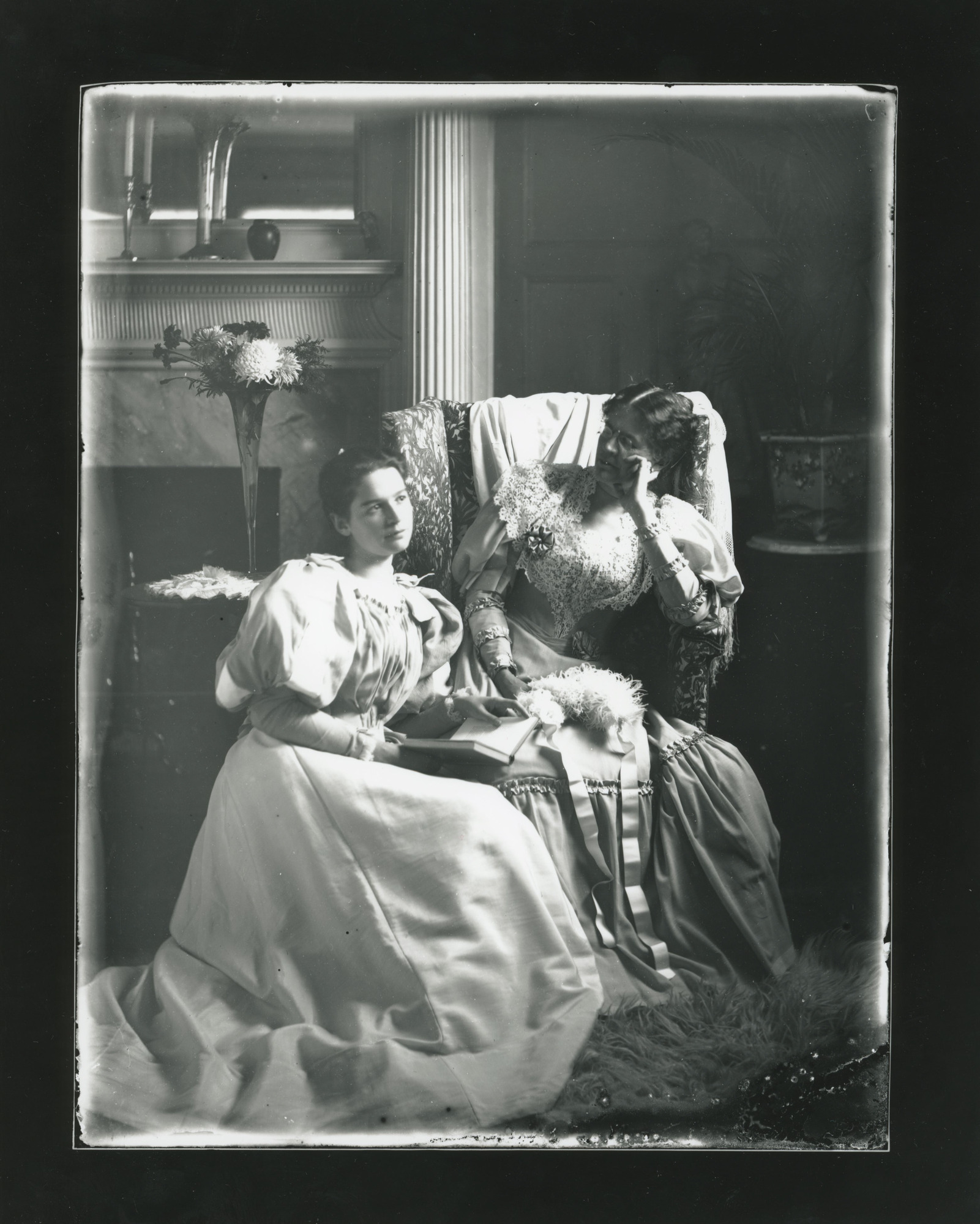 An older white woman wearing eyeglasses sits looking at a younger woman to her right. Younger woman looks up from a book.