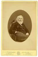 Henry Wadsworth Longfellow seated, with his legs turned to his left, eyes facing the viewer, and his right hand in his pants pocket. Image in oval. Longfellow is wearing a dark vest and jacket and striped trousers. He has almost shoulder-length white hair and a full white/gray beard.