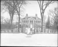 Black and white photograph of Georgian mansion, front fence visible and lawn covered in snow.