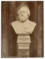 Photograph of Henry Wadsworth Longfellow portrait bust carved in white material. Bust is attached to a stone wall. There is a pedestal beneath it also attached to the wall. Longfellow looks to be wearing a graduation gown. His hair and full beard are carved in detail.