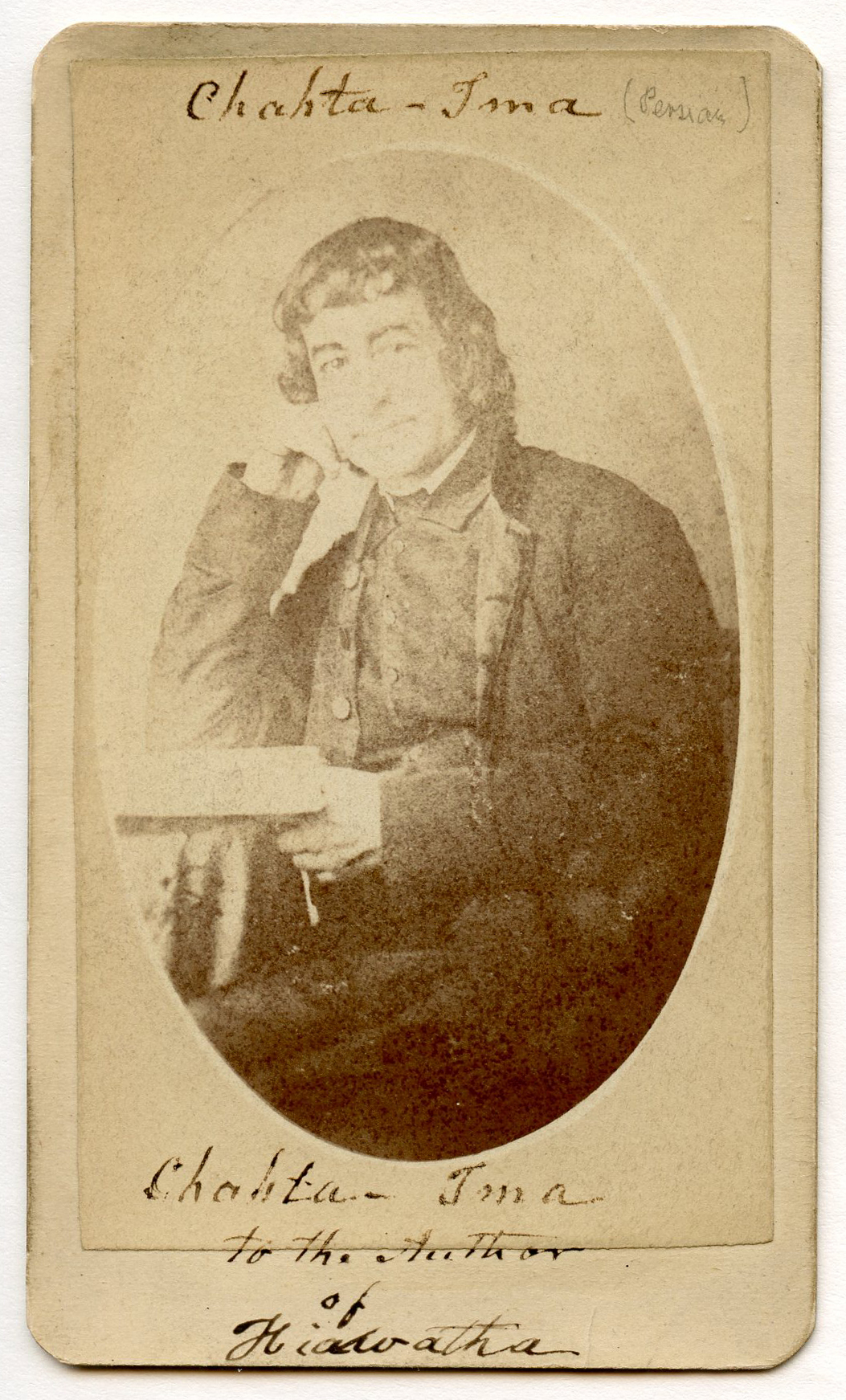 Portrait of a white man. Image in oval shape. Man in Western formal dress sitting and looking directly at viewer. He holds a book with his left hand and leans his head on his right head. His dark hair is cut in short straight bangs across forehead. He seems to be smiling.